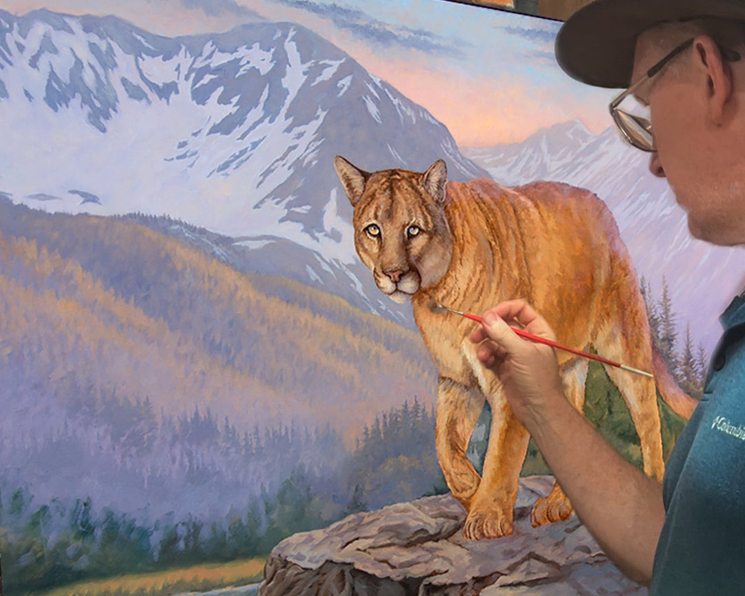 Artist painting a mountain lion scene with mountains and water in the background