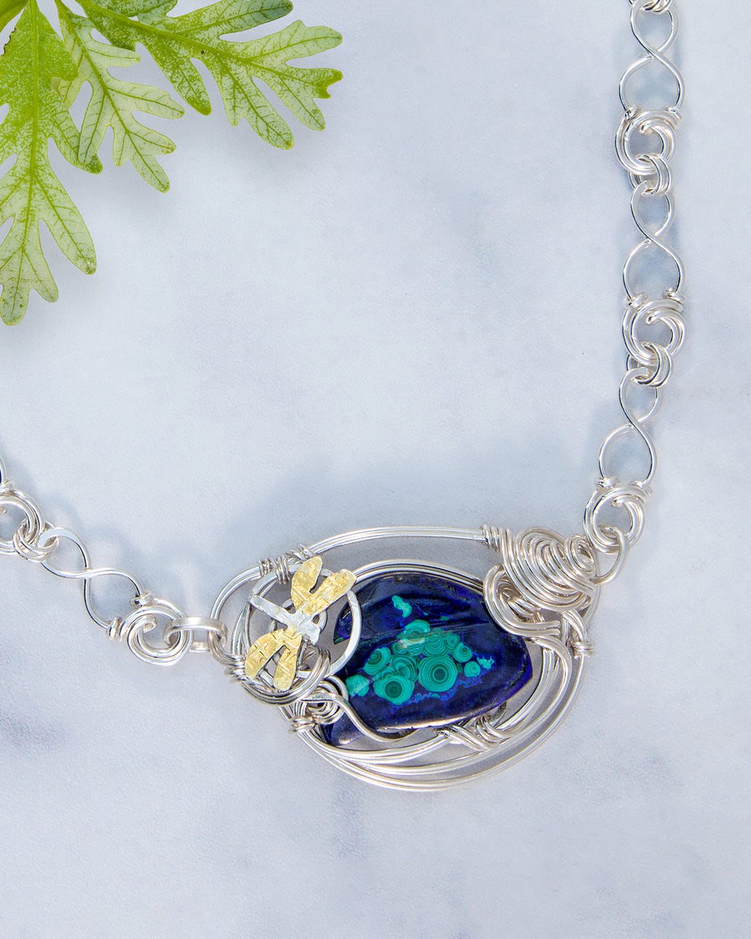 Silver necklace with a blue pendant featuring a dragonfly design on a light gray background.