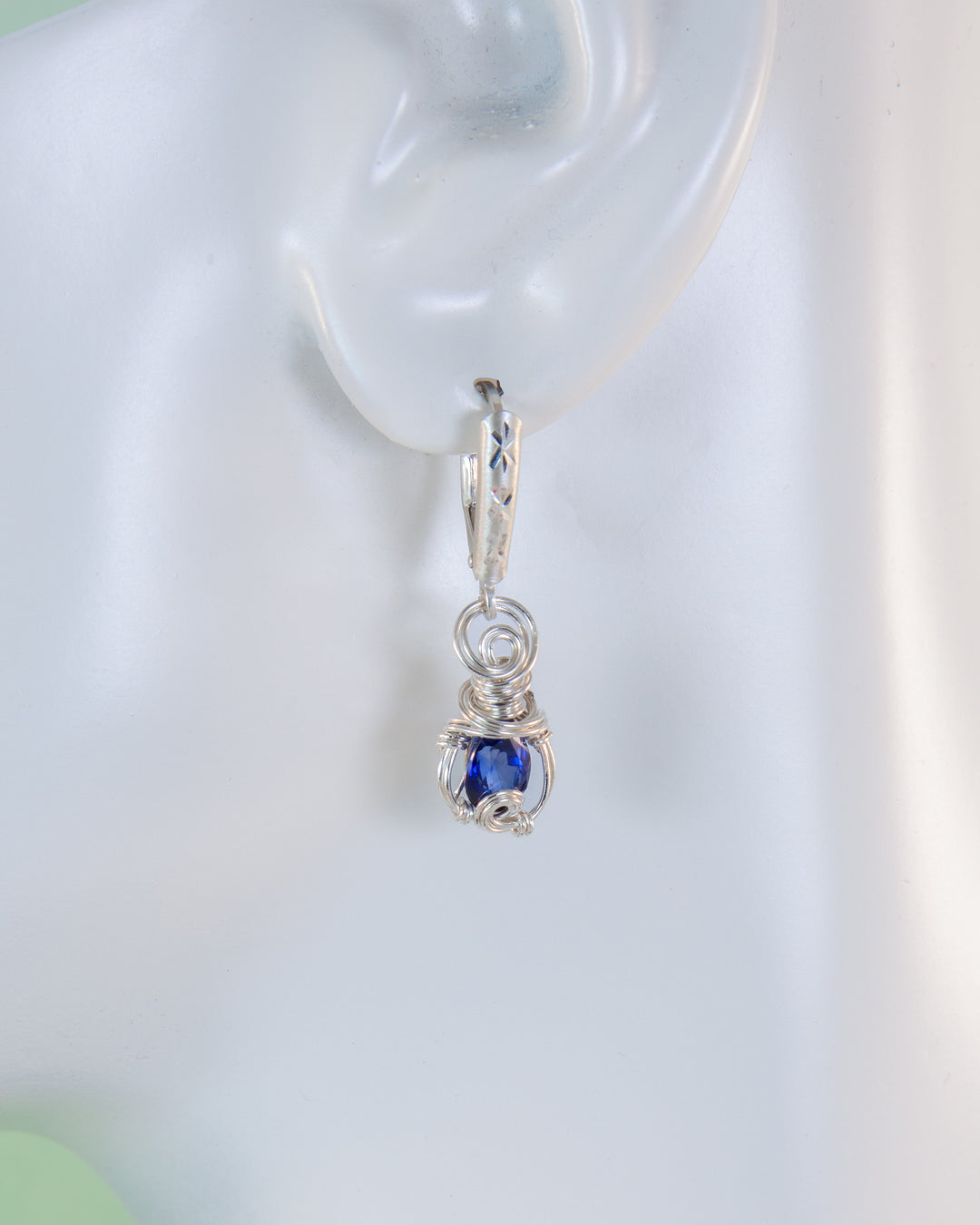 Silver hoop earring with a blue gemstone on a white background