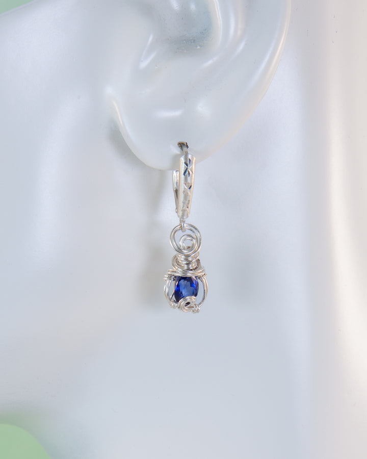 Silver hoop earring with a blue gemstone on a white background