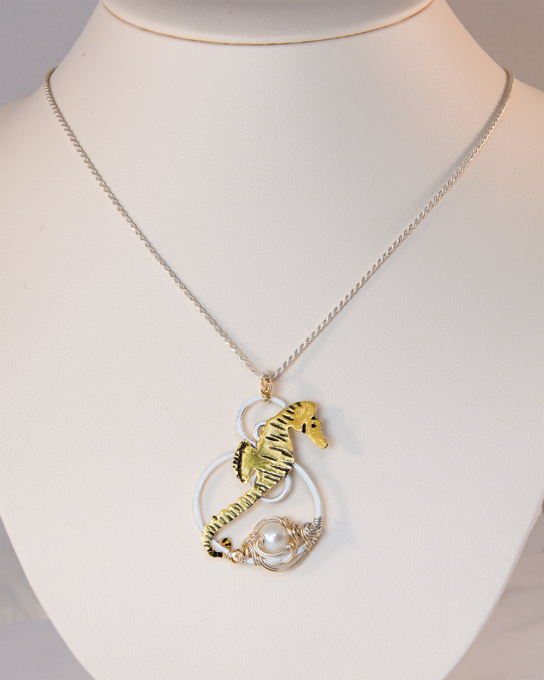 A gold and silver seahorse pendant necklace with a white pearl, displayed on a white mannequin bust.