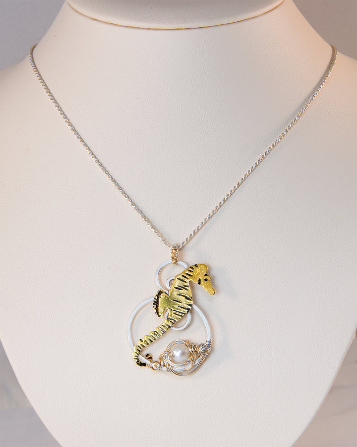 A gold and silver seahorse pendant necklace with a white pearl, displayed on a white mannequin bust.