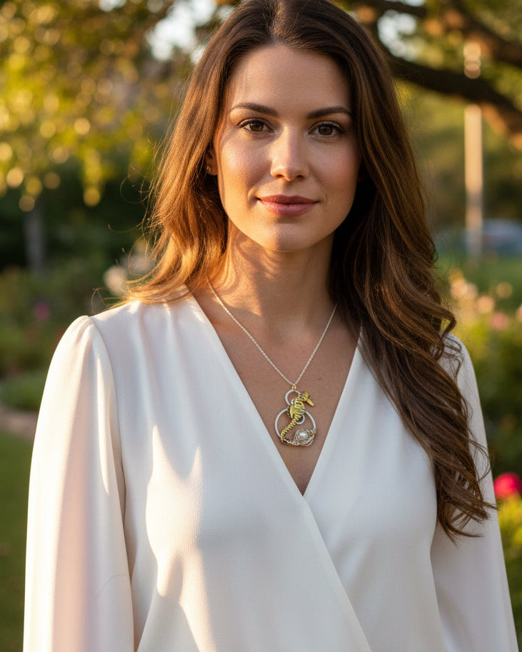 A gold and silver seahorse pendant necklace with a white pearl, displayed on a model