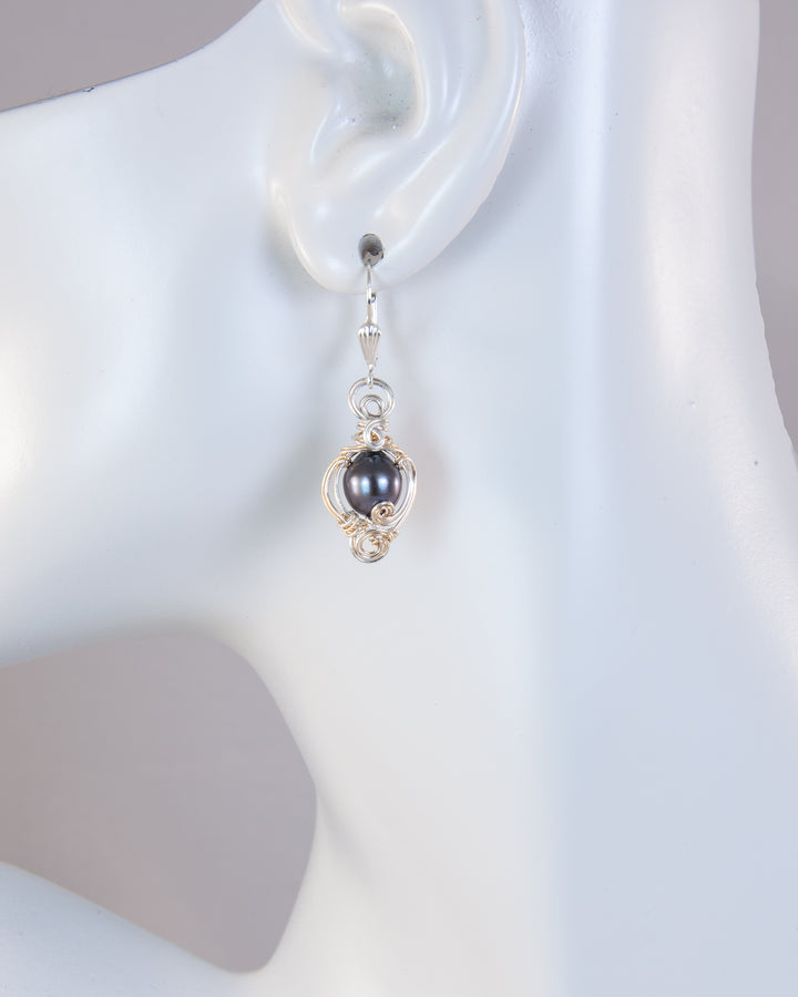 A single dangling earring displayed on a white mannequin ear. The earring features a dark gray pearl set in a silver and gold-filled with sterling silver leverbacks