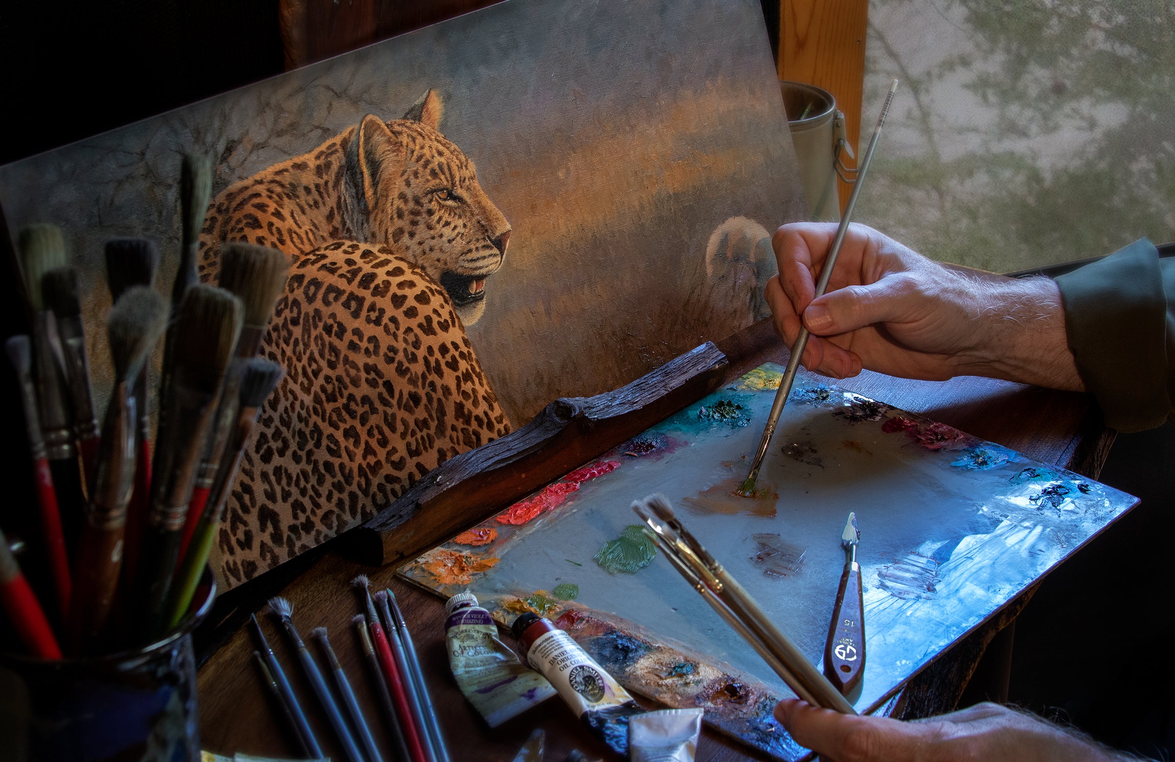 Artist painting a leopard with oil paints and brushes on a canvas.