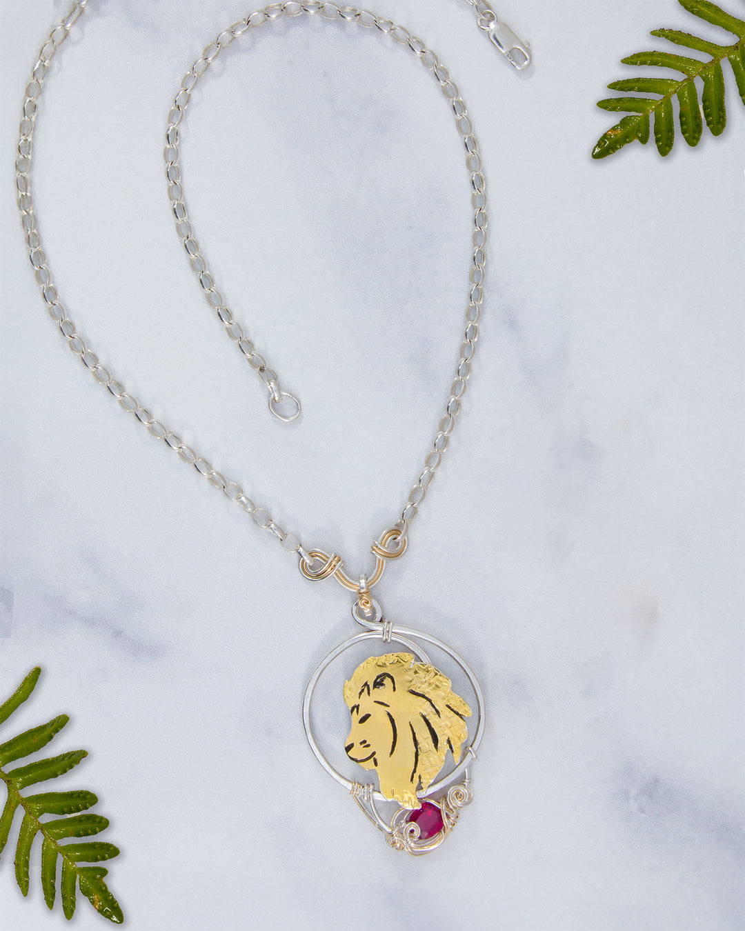Necklace with a lion pendant on a marble surface with green leaves.