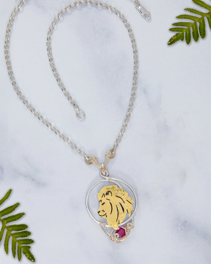 Necklace with a lion pendant on a marble surface with green leaves.