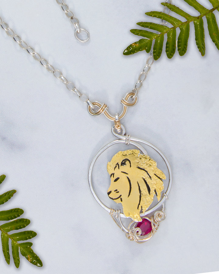 Necklace with a gold lion pendant and red gemstone on a white background with green leaves.